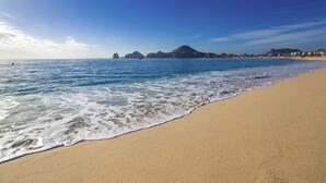 A beach with clear blue water, a sandy shore, and distant hills.