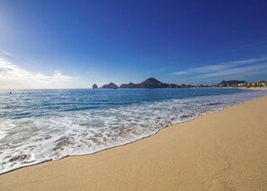 Uma praia com águas azul-claras, areal arenoso e colinas ao longe.
