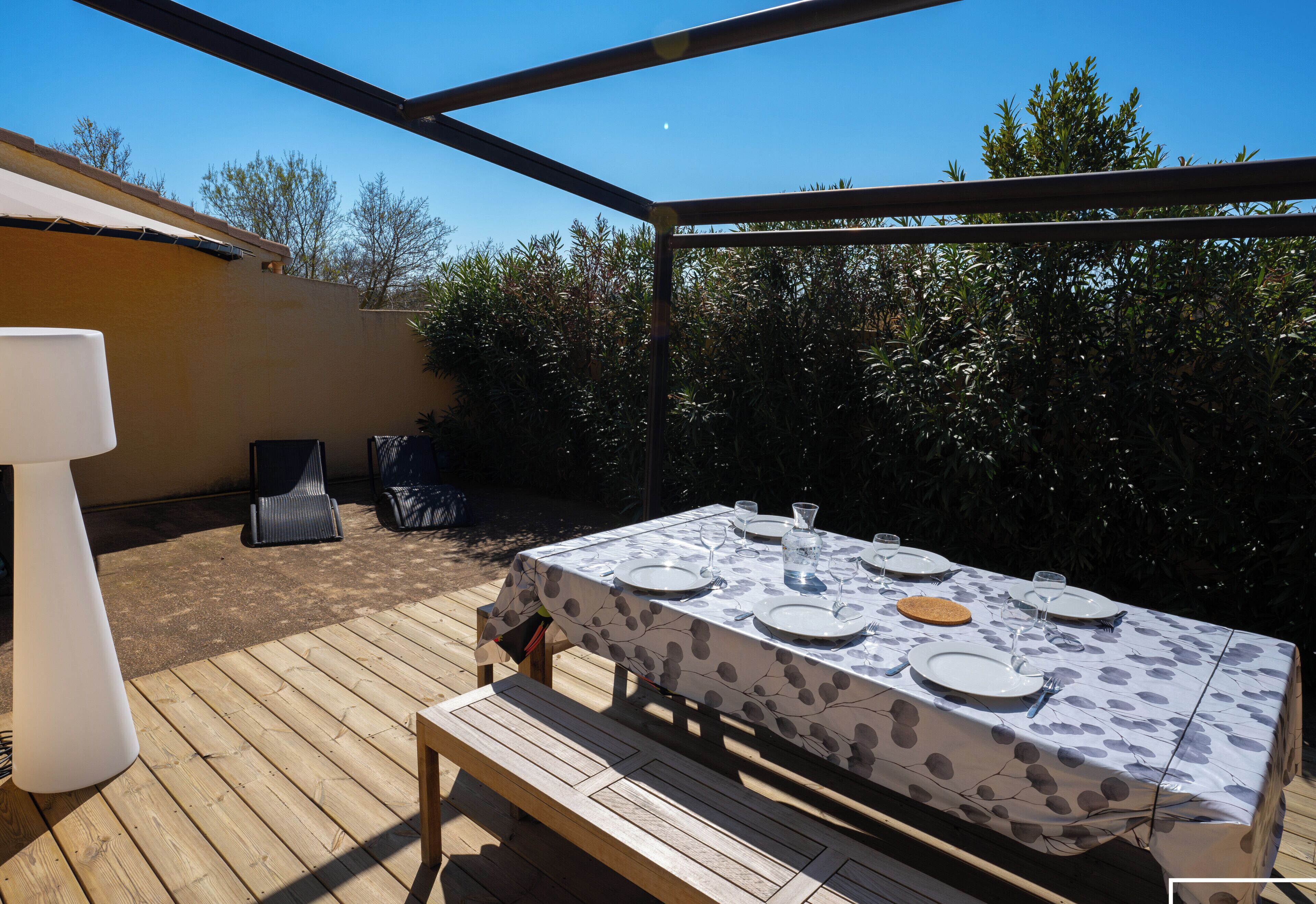 An outdoor dining area with a table set for four, surrounded by a wooden deck and covered by a pergola.