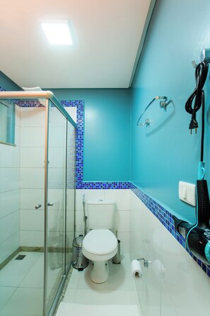 Un baño con cabina de ducha de vidrio, inodoro y lavamanos con perchero para toallas.