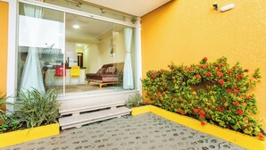 A modern building with a glass entrance, a yellow exterior wall, and a small garden with red flowers.
