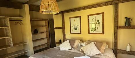 A bedroom with a large bed, wooden beams, a hanging light fixture, and framed botanical prints on the wall.