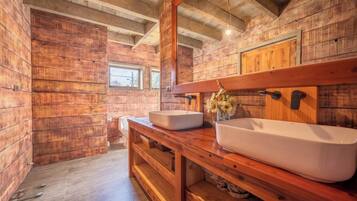 Un baño rústico con paredes de madera, un tocador de madera con dos lavamanos y un espejo sobre el tocador.