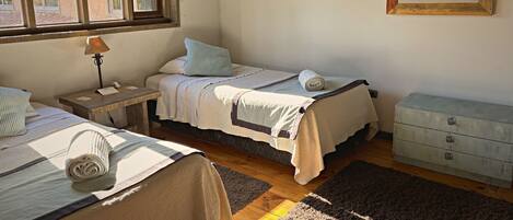 A bedroom with two beds, a nightstand, a dresser, a window with blinds, and a framed picture on the wall.