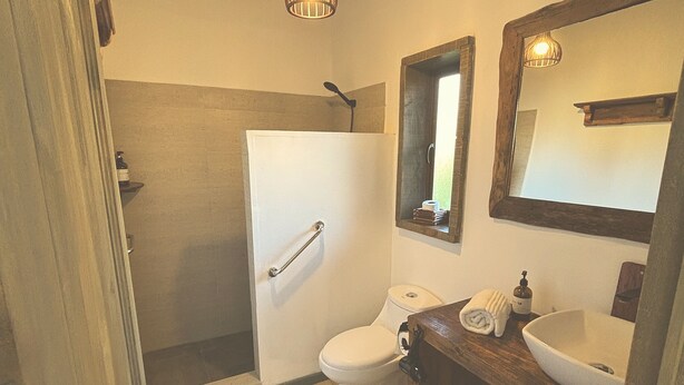 Ein Badezimmer mit Holzboden, Toilette in Weiß, Waschbecken mit Spiegel darüber und einer Duschkabine.