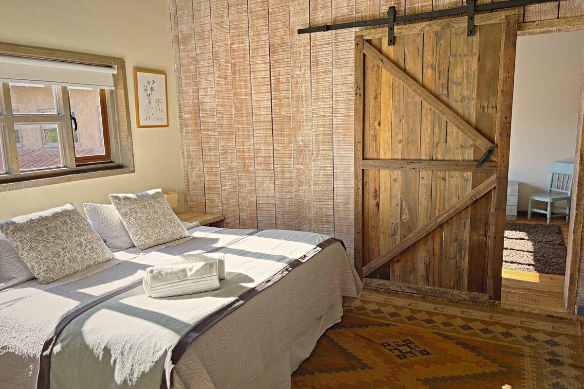 Um quarto com uma cama, porta de madeira, janela e tapete.
