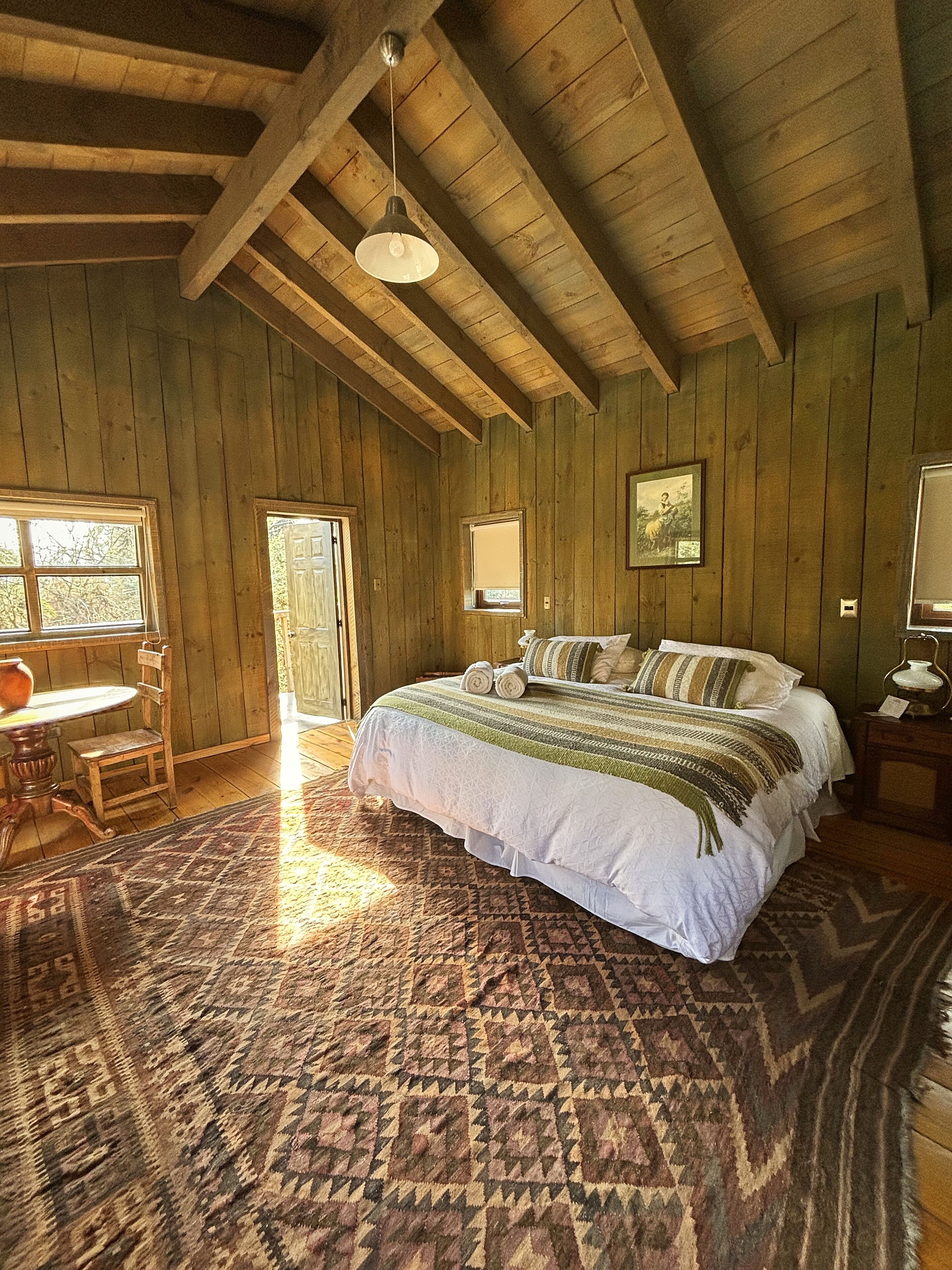 A wooden room with a bed, a table, and a chair.