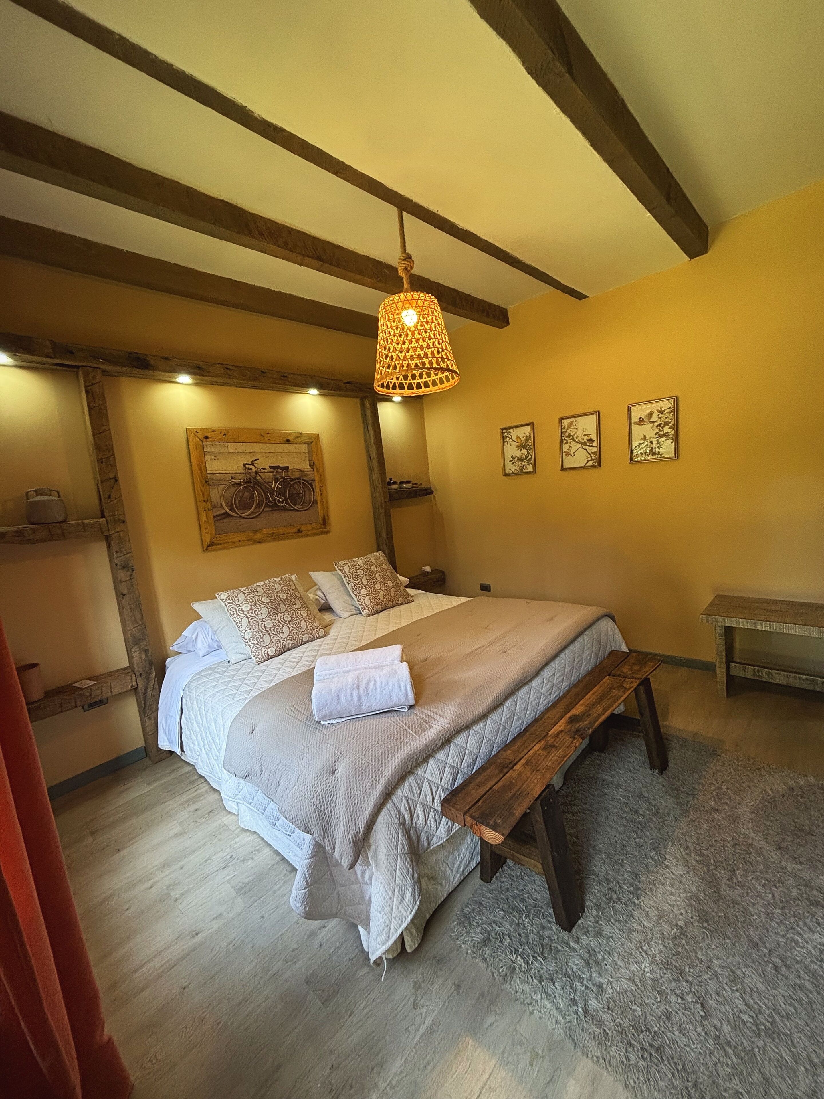 A bedroom with a bed, a bench, a hanging lamp, and wall-mounted artwork.
