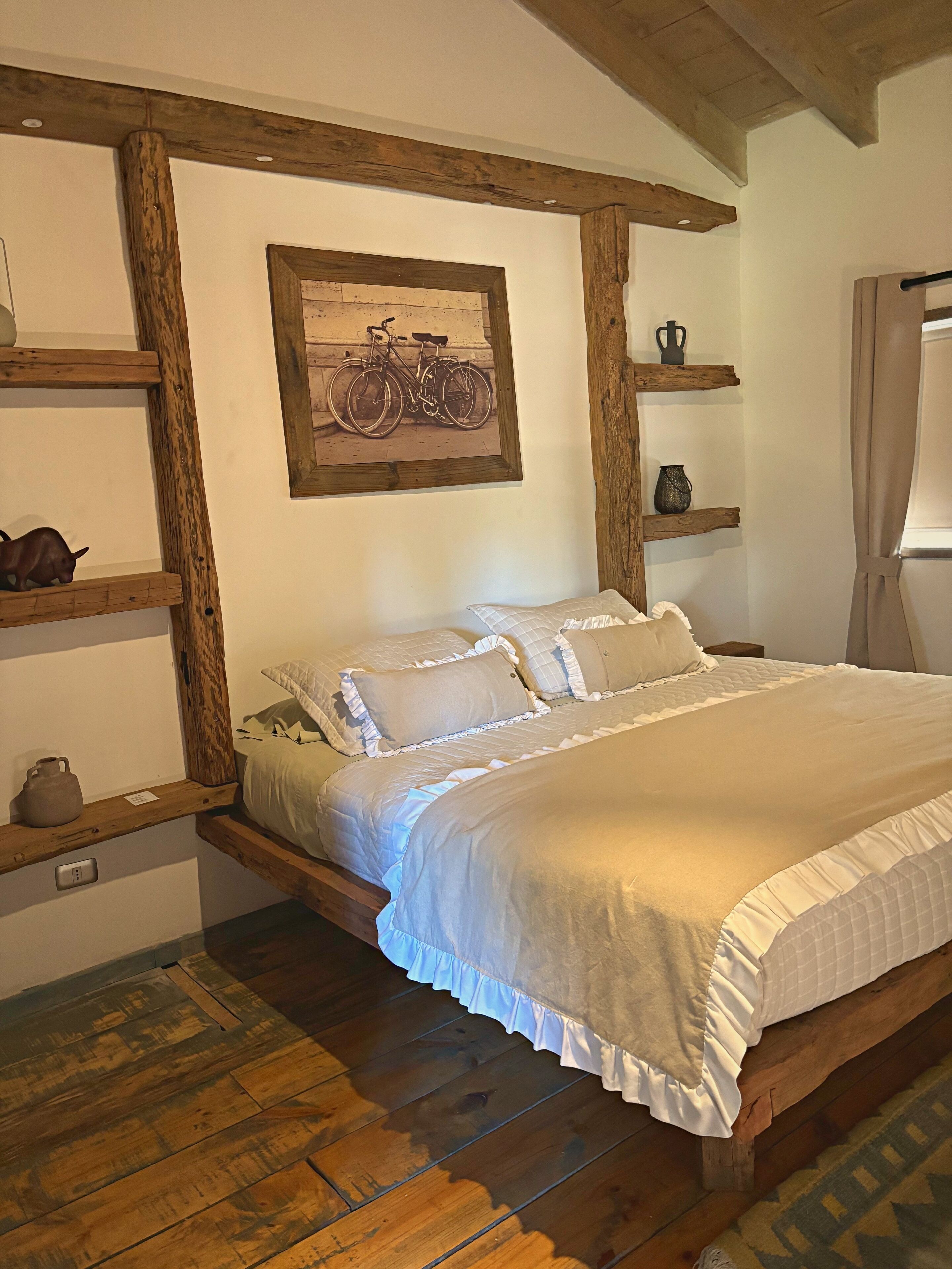 A bedroom with a wooden bed frame, a mounted picture, and wooden shelves with decorative items.