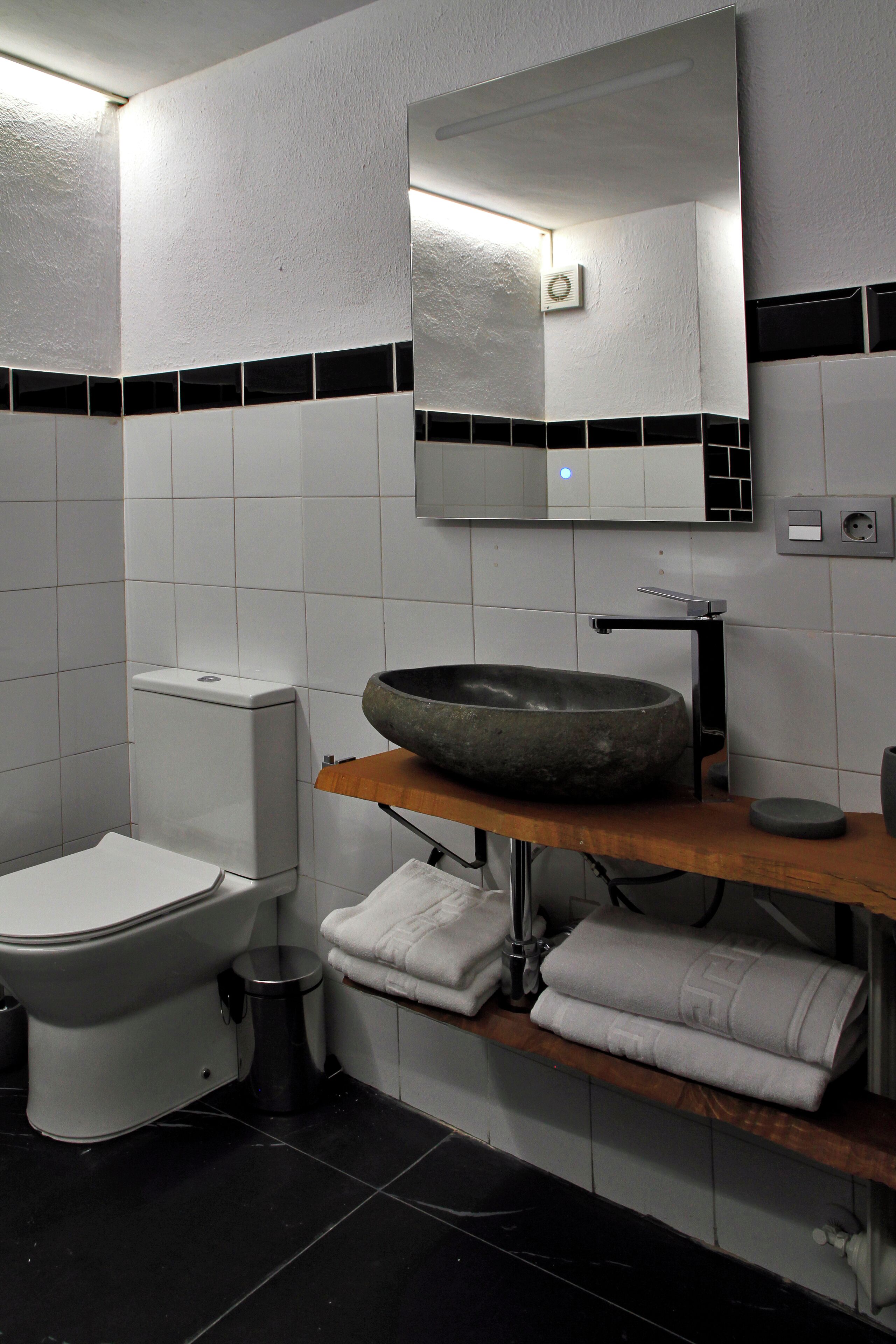 A modern bathroom with a white toilet, a black sink with a round basin, and a mirror above the sink.