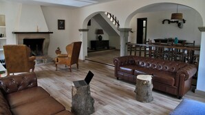 Een ruime woonkamer met een open haard, leren banken, een houten salontafel en een trap naar een hoger gelegen verdieping.