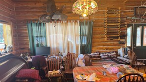 Interior acogedor de una cabaña con una mesa de comedor, sillas, un sofá, un piano y una araña.
