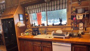 Una cocina con armarios de madera, un refrigerador negro, un lavavajillas y una ventana con un adorno a cuadros.
