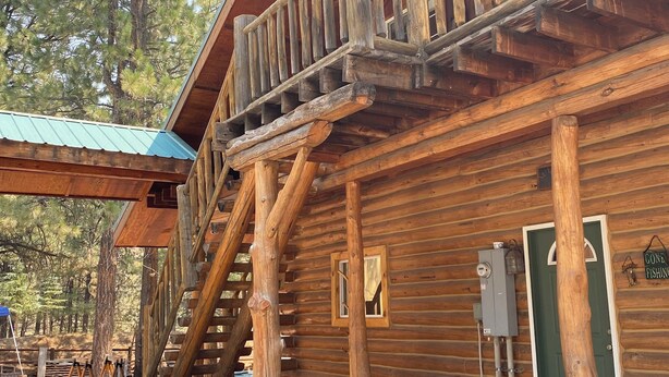 Una cabaña de troncos con un balcón de madera, una escalera y una puerta verde.