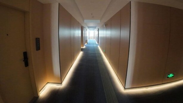 A long, narrow hotel corridor with a carpeted floor and walls on both sides.