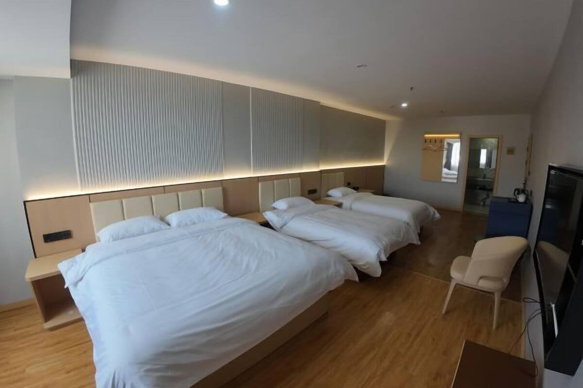 Ein Hotelzimmer mit drei Betten, einem Fernseher, einem Schreibtisch und einem Stuhl.