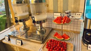 A beverage station with two dispensers, a tray of cherry tomatoes, and a display of watermelon slices.