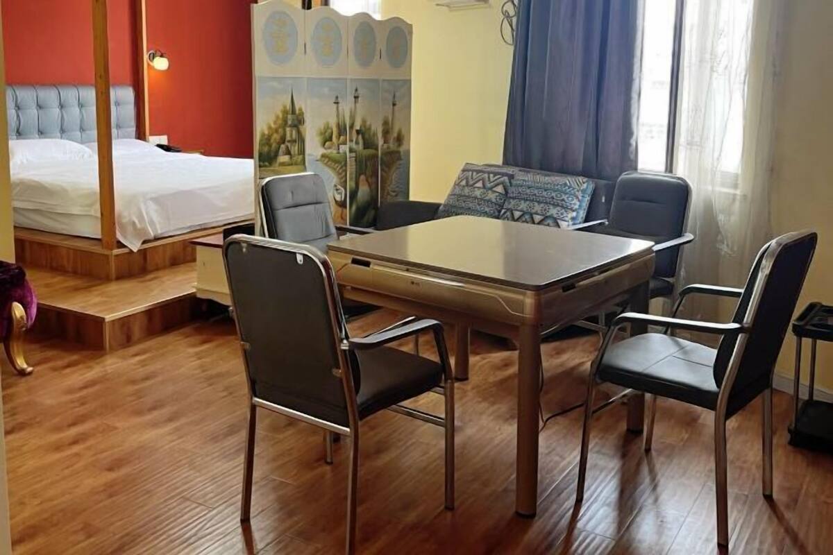 Ein Zimmer mit einem Bett, einem Esstisch mit Stühlen, einem Bild an der Wand und einem Fenster mit Vorhängen.