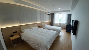 A hotel room with two beds, a small bedside table, a TV, and a window with curtains.