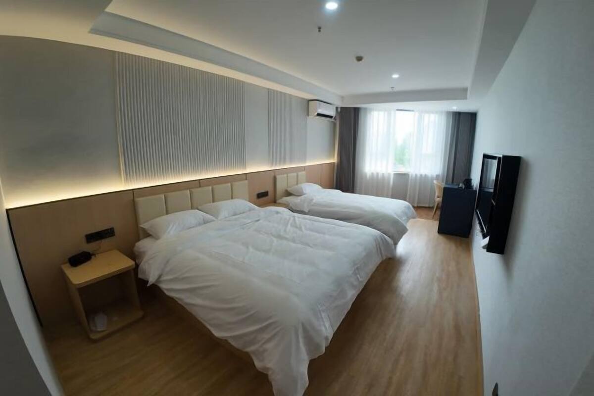 Ein Hotelzimmer mit zwei Betten, einem kleinen Nachttisch, einem Fernseher und einem Fenster mit Vorhängen.