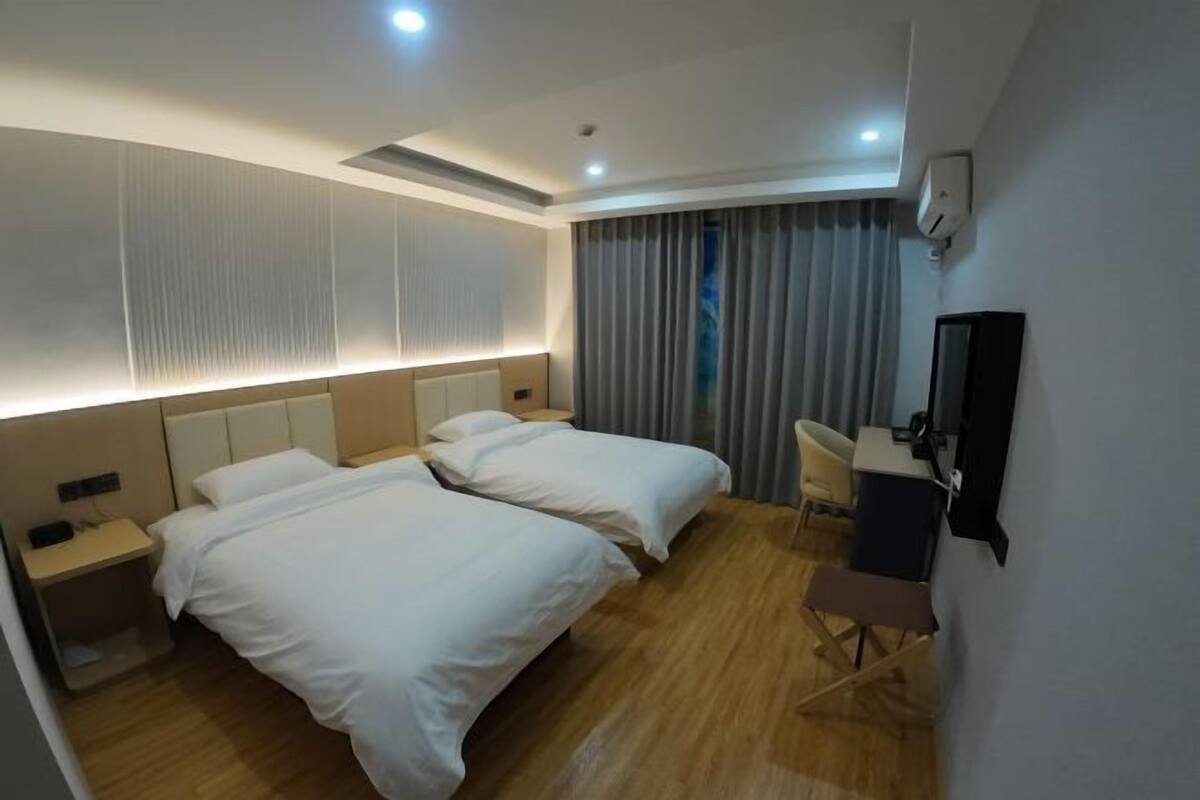 Ein Hotelzimmer mit zwei Betten, einem Schreibtisch, einem Stuhl, einem Fernseher und einem Fenster mit Vorhängen.