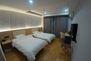 A hotel room with two beds, a desk, a chair, a TV, and a window with curtains.