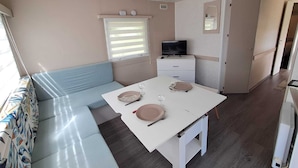 Une pièce de taille modeste, avec une table blanche, un canapé bleu, un téléviseur posé sur une commode et un miroir accroché au mur.