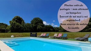 Une piscine équipée de chaises longues et d’un panneau indiquant qu’elle est à usage partagé, ouverte de mai à septembre, sous réserve de conditions météorologiques favorables.
