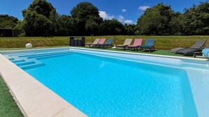 Una piscina rectangular con superficie de agua azul cristalina, rodeada por una solana empavedada. Varias sillas de descanso con cojines de diferentes colores están alineadas a lo largo del borde de la piscina.