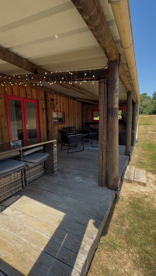 Un espacio de estar al aire libre cubierto con muebles de madera y luces colgantes.