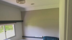 Una habitación con un escritorio blanco, una silla azul, un tapete tejido y una ventana con persianas.