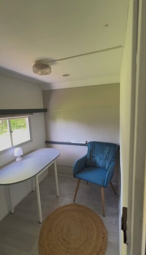 A room with a white desk, a blue chair, a woven rug, and a window with blinds.
