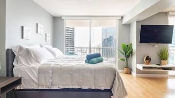 Une chambre moderne avec un grand lit, un téléviseur fixé au mur et un balcon offrant une vue sur la ville.