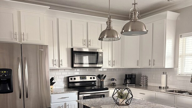 A modern kitchen with white cabinetry, stainless steel appliances, and a granite countertop island.