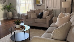 A living room with a beige sofa, a coffee table, a potted plant, and a ceiling fan.