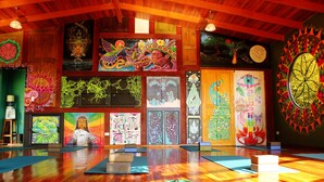 A spacious room with wooden floors, colorful artwork on the walls, and yoga mats on the floor.