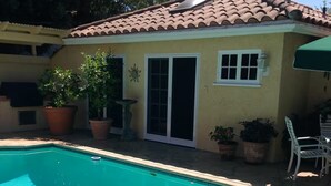 A swimming pool with a tiled deck, a patio area with potted plants, and a building with a tiled roof and sliding glass doors. - Safe & beautiful new studio in charming Sherman Oaks neighborhood (Los Angeles)