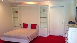A bedroom with a bed, red carpet, white walls, and built-in shelving. - Safe & beautiful new studio in charming Sherman Oaks neighborhood (Los Angeles)