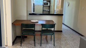 A compact kitchen with a wooden table and two chairs, a microwave, and a hanging light fixture. - Centro da cidade tudo a pé (Cabo Frio)