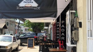 An outdoor seating area with tables and chairs, a sign for 'Padaria Lanchonete', and parked cars along the street. - Centro da cidade tudo a pé (Cabo Frio)