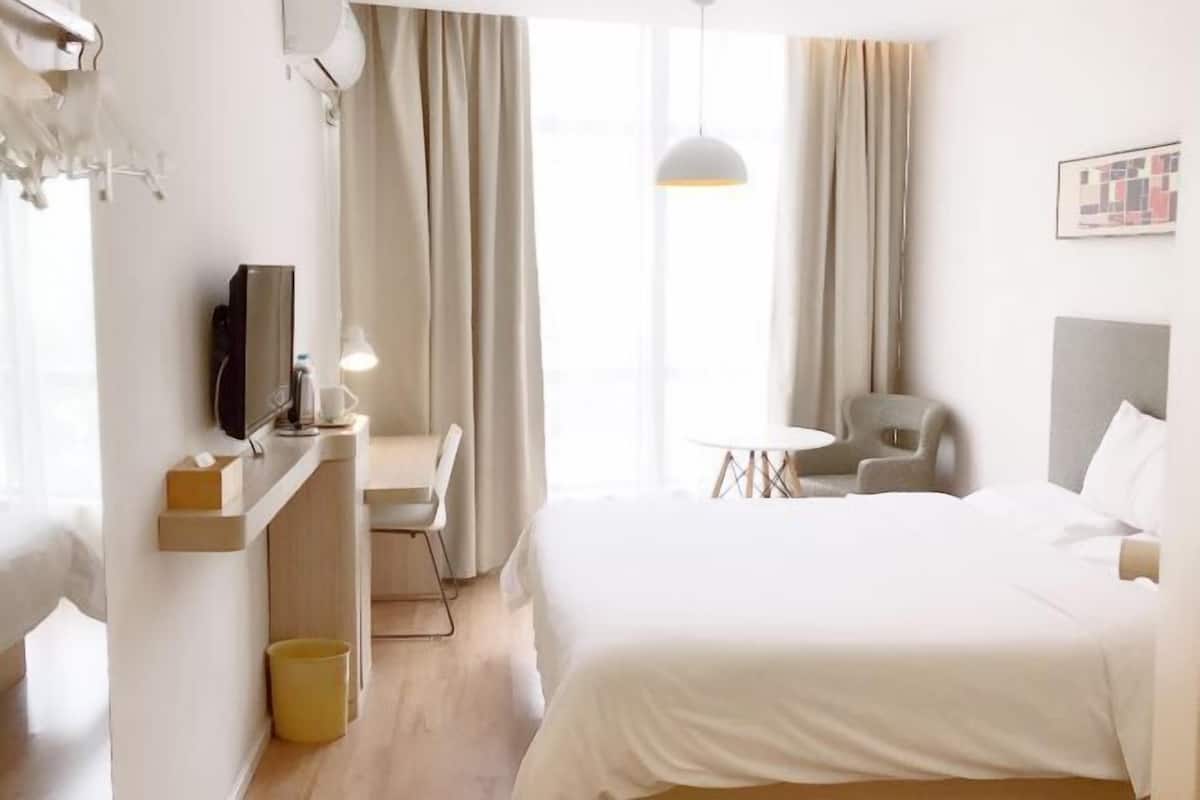 A hotel room with a bed, a desk with a chair, a small table, and a TV.