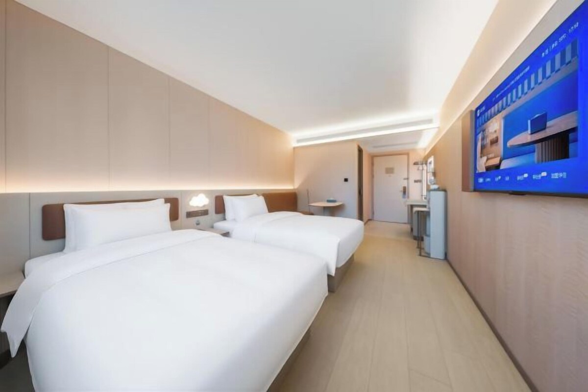 A hotel room with two beds, a desk, and a television on the wall.