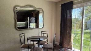 A dining area with a round table and four chairs, a large mirror on the wall, and a view of a backyard through a sliding glass door. - Charming 2-bedroom pet-friendly house with fenced yard minutes from Galveston! (Hitchcock)