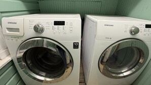 Two Samsung front-loading washing machines in a room with green walls and wooden flooring. - Charming 2-bedroom pet-friendly house with fenced yard minutes from Galveston! (Hitchcock)