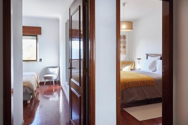 A hallway leading to a bedroom with a bed, a chair, and a window.