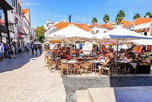 Enjoy a meal or coffee in a charming outdoor setting with tables and chairs shaded by umbrellas.