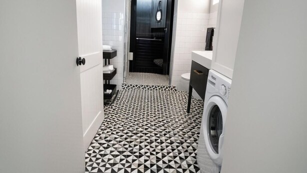 Een kleine badkamer met een zwart-wit geometrisch vloertapijt, een wasmachine en een toilet.