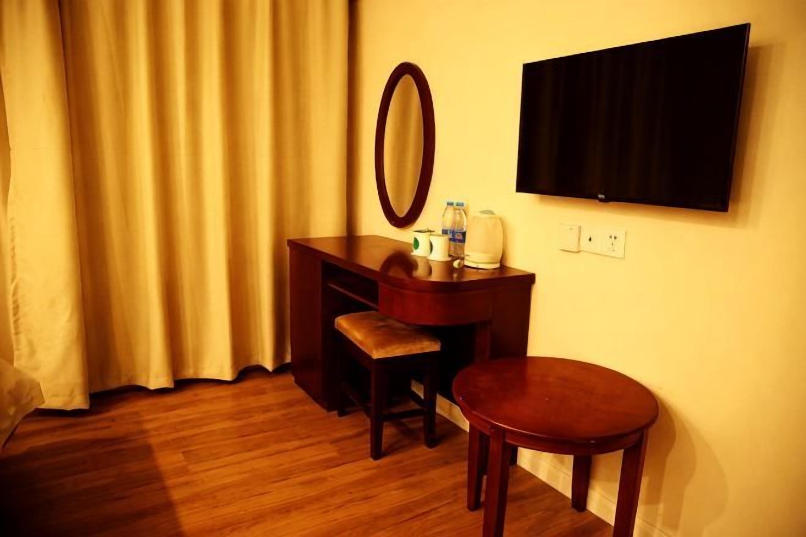 A hotel room with a wooden desk, a chair, a round table, a mirror, and a flat-screen TV mounted on the wall.