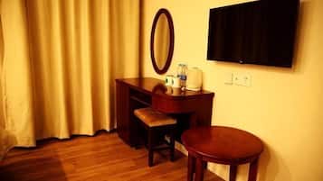 A hotel room with a wooden desk, a chair, a round table, a mirror, and a flat-screen TV mounted on the wall.