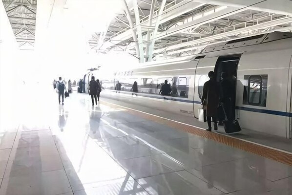 A train station platform with a train, passengers, and a covered roof structure.